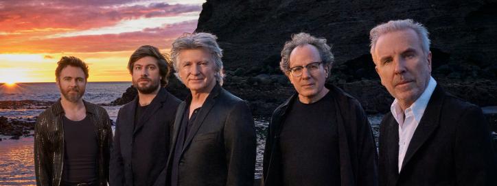 Members of the band Crowded House pose on a beach at sunset