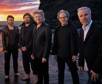 Members of the band Crowded House pose on a beach at sunset