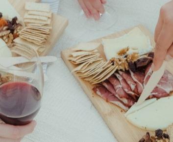 Image of hands holding red wine and cutting cheese