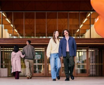 Modern gallery entrance with visitors walking past a large orange sculpture and contemporary artwork.
